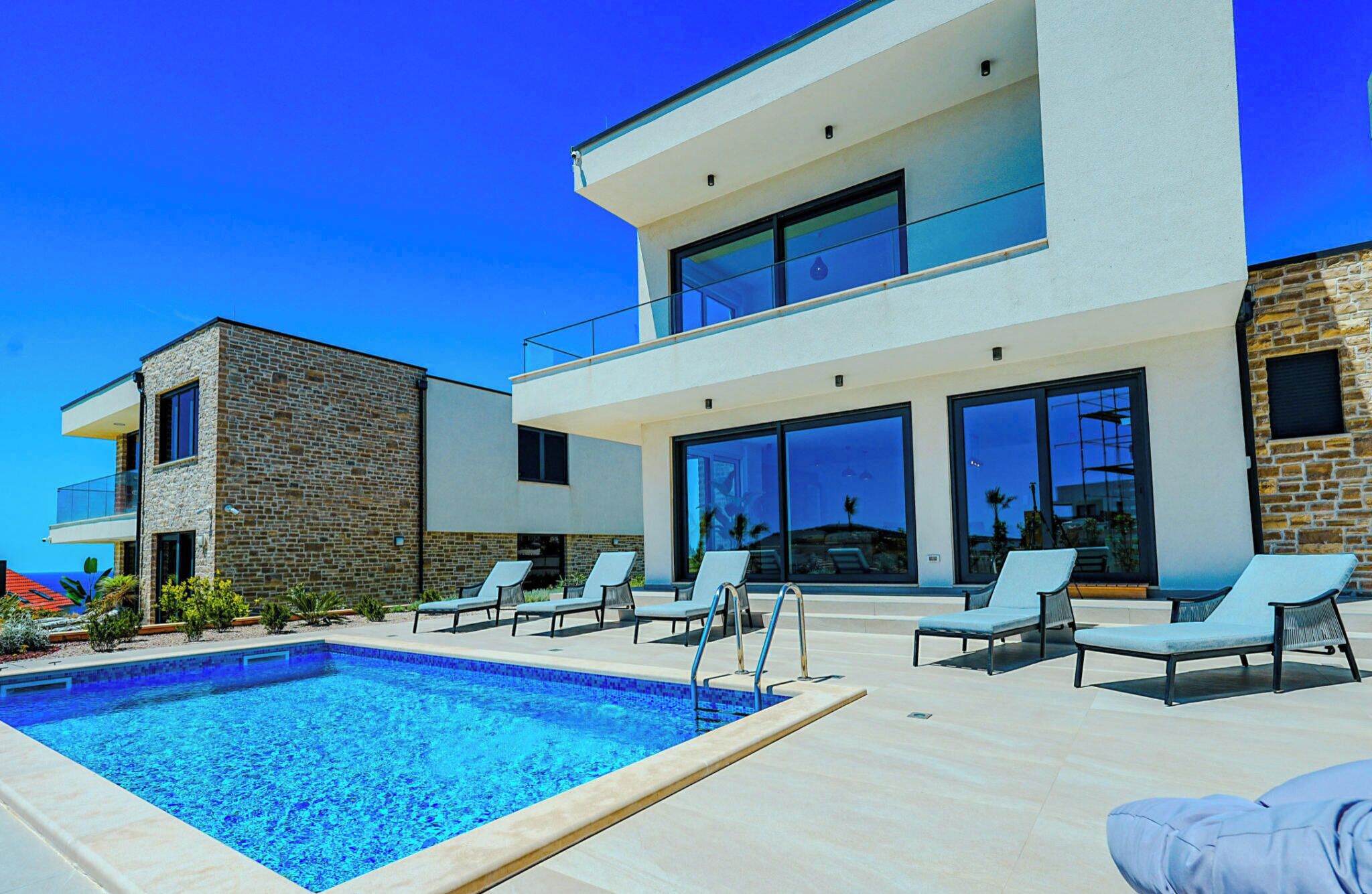 Ein modernes, zweistöckiges Haus mit Schwimmbad und Sitzgelegenheit im Freien.