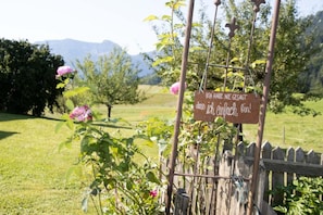 A sign with text in a foreign language, a wooden fence, and a garden with pink flowers and green grass. - Vacation apartment Guat'kammer (Inzell)