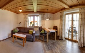 A room with a wooden ceiling, a sofa, a table, and a window with curtains. - Vacation apartment Guat'kammer (Inzell)