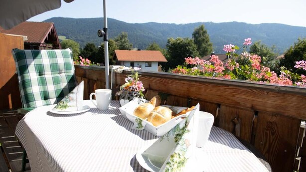 A table set outdoors with a view of mountains, a wooden fence, and flowers. - Vacation apartment Guat'kammer (Inzell)