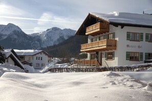 A chalet-style building with a wooden balcony, surrounded by snow-covered mountains. - Vacation apartment Guat'kammer (Inzell)