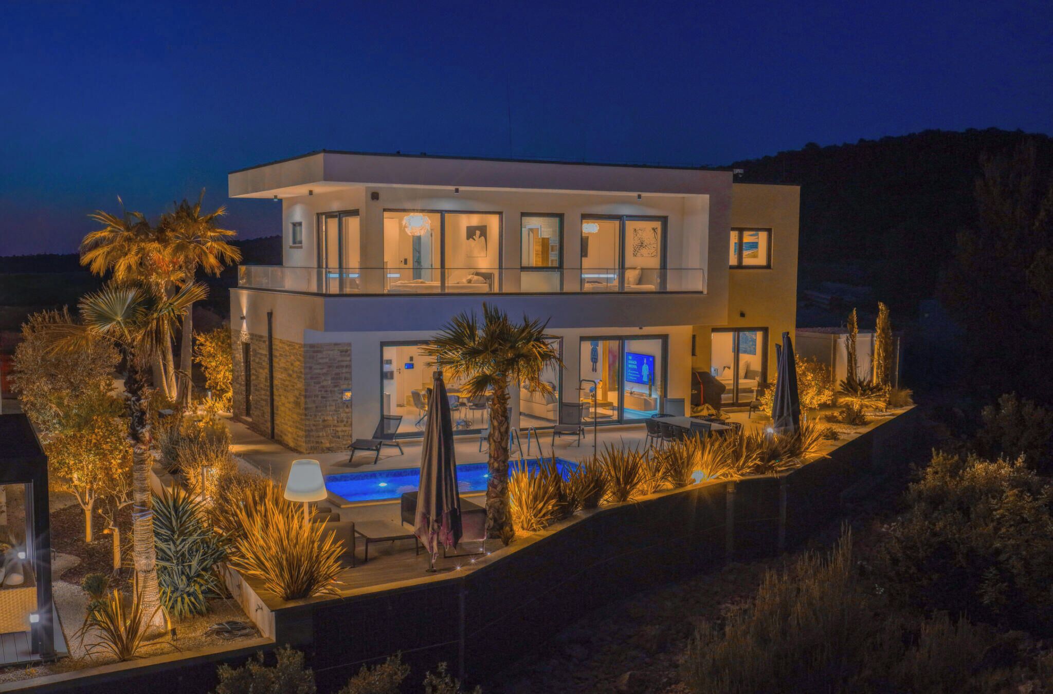A modern two-story house with a swimming pool, surrounded by landscaped gardens and palm trees.