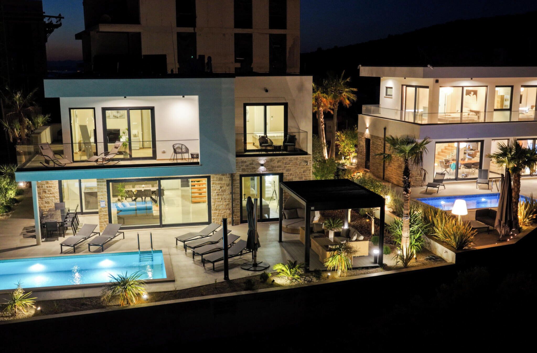 Une maison moderne à deux étages, dotée d  ’une piscine, d’un espace extérieur aménagé et d’un patio bien éclairé.
