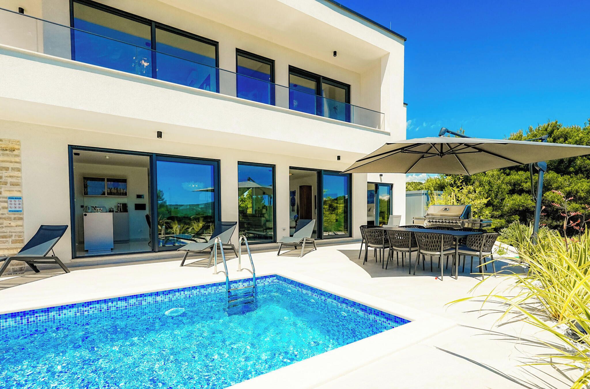 Ein modernes, zweistöckiges Gebäude mit Swimmingpool, Außenbereich zum Sitzen und Grillplatz.
