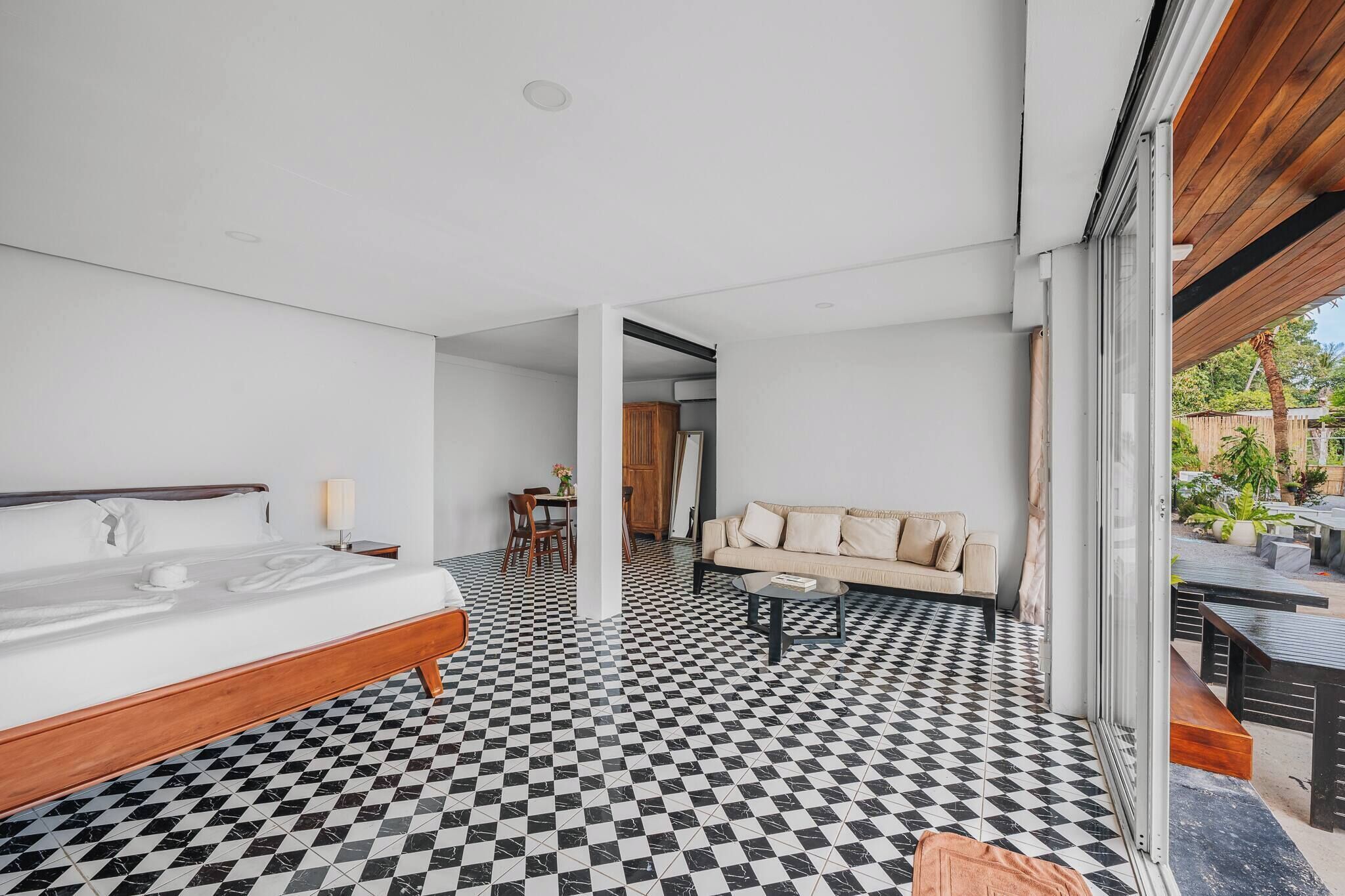 A modern hotel room with a checkered floor, a bed, a sofa, and a dining area.