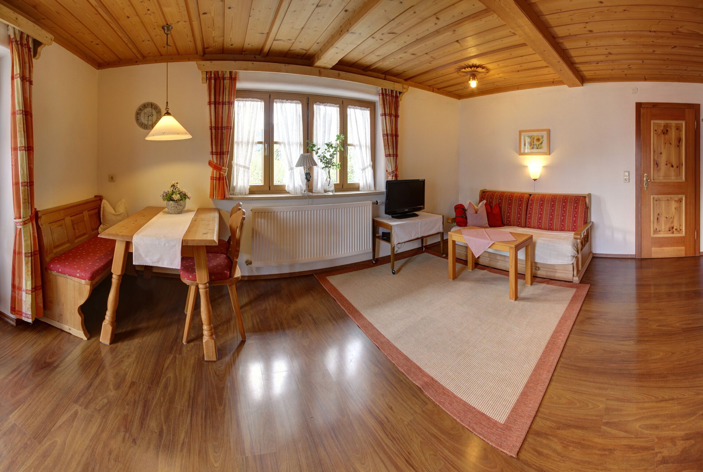 A cozy room with wooden floors, a dining table with chairs, a sofa, a television, and a radiator.