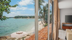 Une chambre dotée d’une grande porte-fenêtre coulissante donnant sur la plage, d’un lit, d’une télévision et d’une armoire en bois.