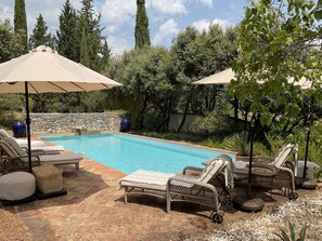Ein Pool mit Liegestühlen und Sonnenschirmen, umgeben von Steinmauern und viel Grün.