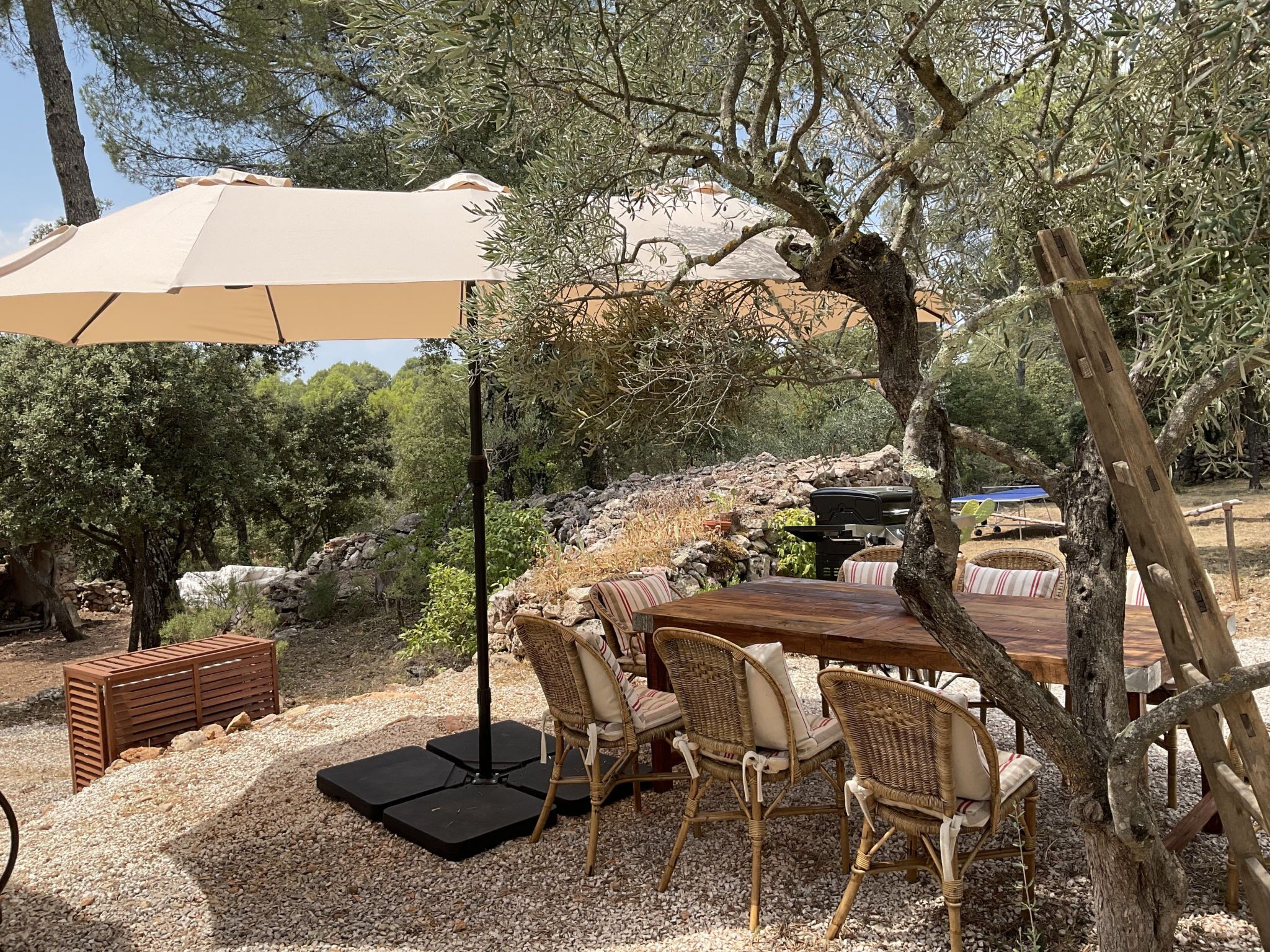 Een buiten eethoek met een tafel, stoelen, een grote parasol en een barbecue.