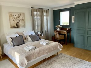 Ein Schlafzimmer mit Bett, Nachttisch, Stuhl, Schreibtisch und einem Fenster mit Vorhängen.