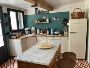 Eine kleine Küche mit einer zentralen Kochinsel, einem Kühlschrank und einem Fenster.