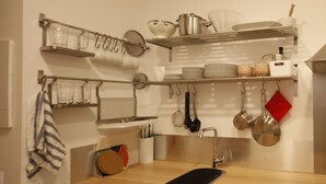 A kitchen with shelves holding dishes, pots, and utensils.