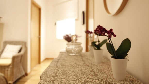 A hallway with a patterned rug, a wicker chair, and potted plants.