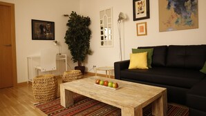 A living room with a black sofa, a wooden coffee table with apples, a potted plant, and a large mirror.