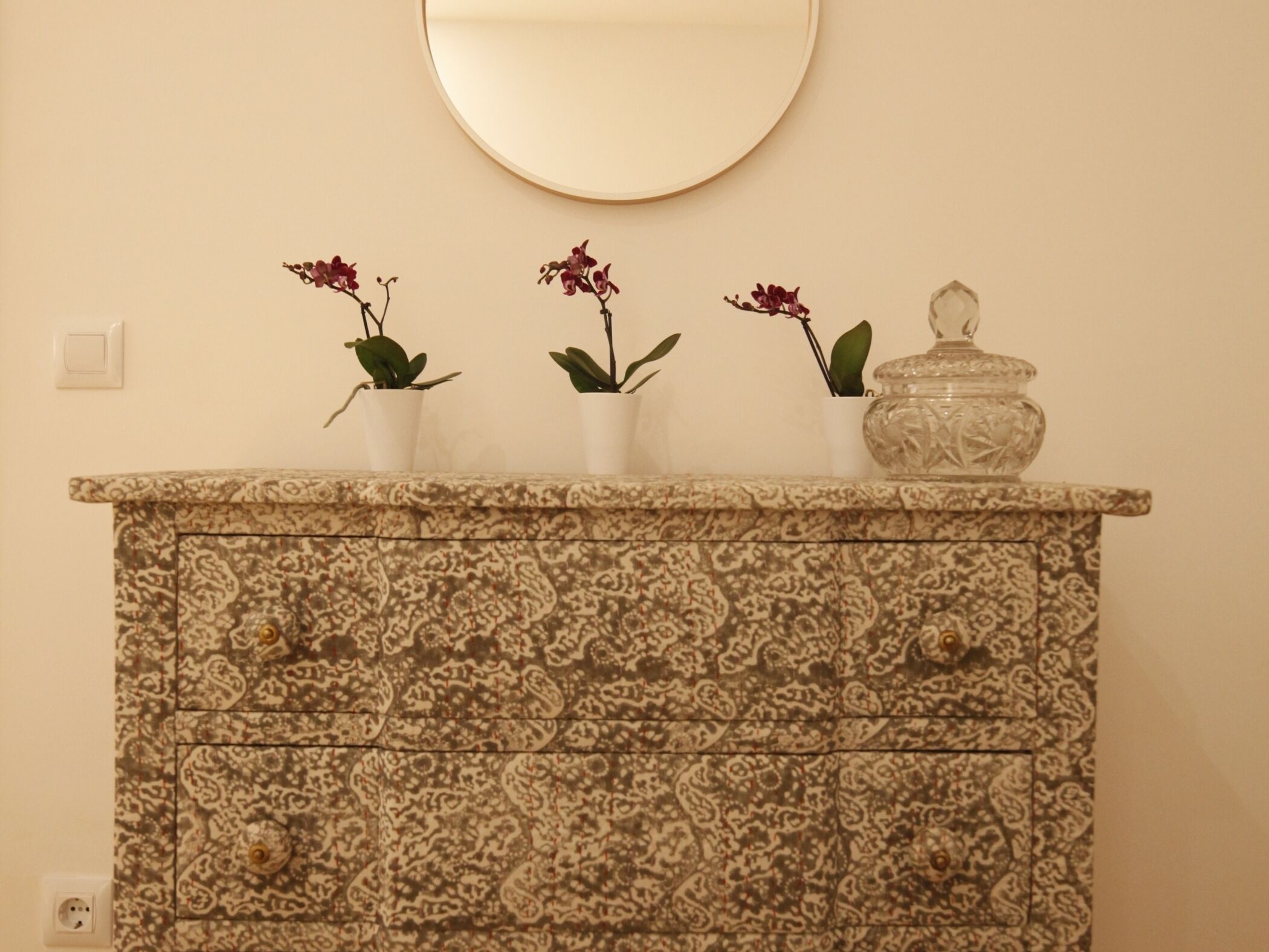 A patterned cabinet with three potted plants and a decorative jar.
