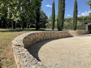 A stone retaining wall with a gravel path curving around it, surrounded by trees and a clear sky. - LI SIAN BEN by Interhome (Carces)