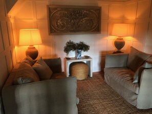 Uma sala de estar acolhedora com dois sofás, uma mesinha lateral, um vaso decorativo e duas luminárias.