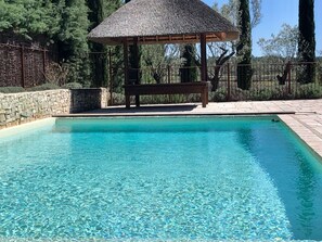 A clear swimming pool with a wooden bench and a thatched-roof gazebo. - LI SIAN BEN by Interhome (Carces)