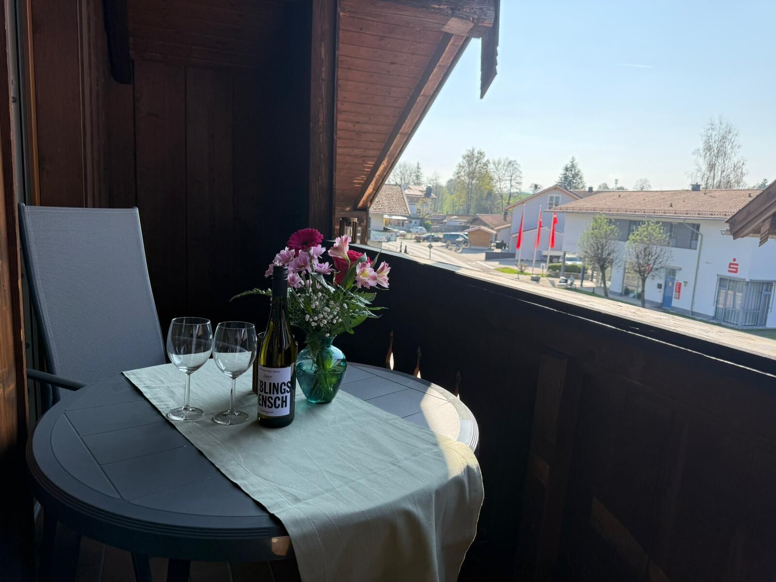 A balcony with a table set for two, a bottle of wine, and a vase with flowers.