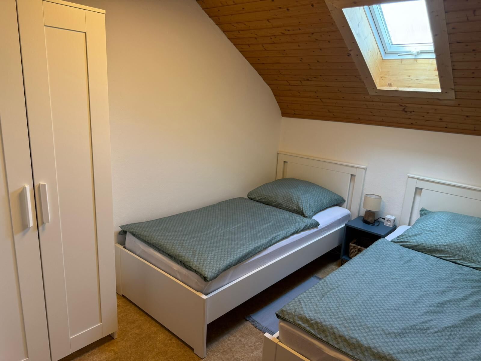 A bedroom with a single bed, a nightstand, a lamp, and a wardrobe.