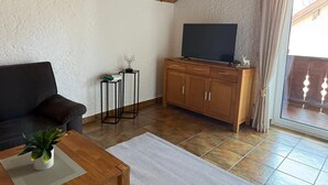 A living room with a sofa, a coffee table with a plant, a TV on a wooden cabinet, and a sliding glass door leading outside. - Vacation apartment BergZeit for max. 4 adults (Chieming)