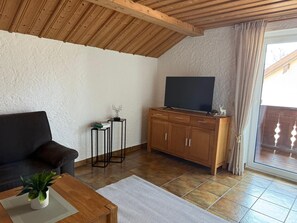 A living room with a sofa, a coffee table with a plant, a TV on a wooden cabinet, and a sliding glass door leading outside. - Vacation apartment BergZeit for max. 4 adults (Chieming)