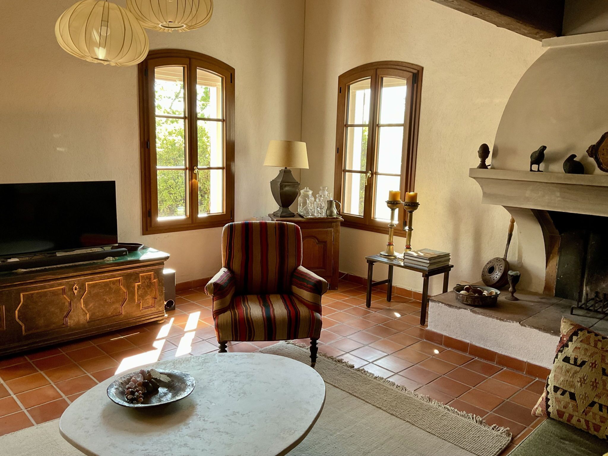 A living room with a television, a striped armchair, a table with books, and a fireplace.