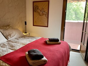 Ein Hotelzimmer mit Bett, einem Gemälde an der Wand, einem Nachttisch und Blick nach draußen.