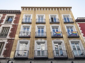 A multi-story building with a yellow facade, white window frames, and black balcony railings. - Apartamento en Puerta del Sol centro ciudad (Madrid)