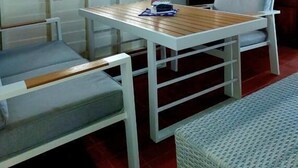 Een kamer met een houten tafel, twee stoelen, een kleine koelkast en een raam met gordijnen.
