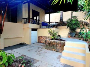 A covered outdoor area with a stone planter, a concrete bench, and a building with a balcony.