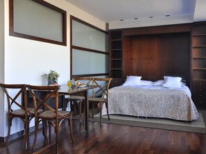 A bedroom with a bed, a dining table with chairs, and a large window. - Luxury Apartment in Plaza de Colon (Madrid)