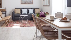 Un soggiorno moderno con un divano grigio, poltrone in vimini, un tavolo da pranzo in legno e un quadro raffigurante un panorama urbano.