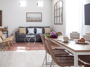 Ein modernes Wohnzimmer mit grauem Sofa, Korbstühlen, einem Holzesstisch und einem Stadtbild an der Wand.