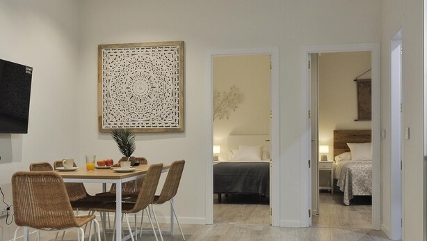 Un'area pranzo con tavolo, sedie e un elemento decorativo a parete. Nella stanza adiacente, un letto e un comodino.