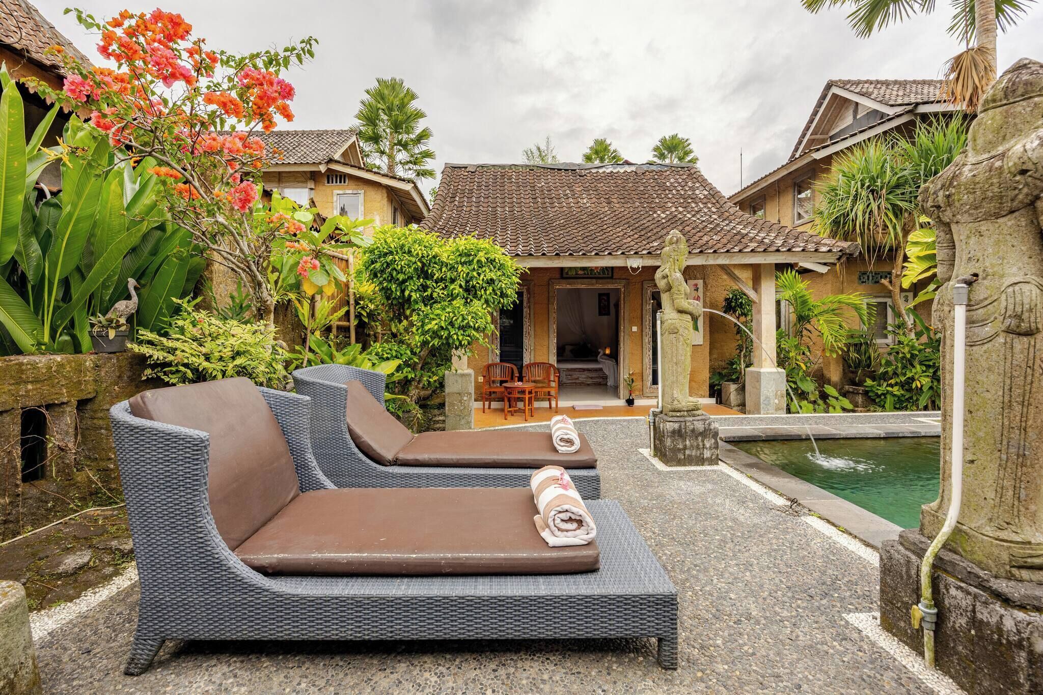A courtyard with two lounge chairs, a small pool, and a stone statue.