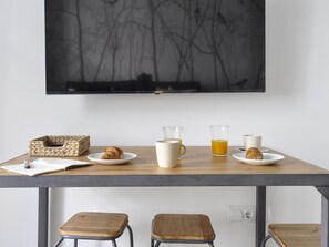 A breakfast setup with croissants, coffee, and juice on a table, with a TV above and stools below. - Apartamento en Puerta del Sol centro ciudad (Madrid)