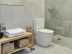 Un baño moderno con inodoro, ducha, taburete de madera y una planta.