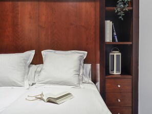 A bed with white linens, a bedside table with a book and glasses, and a wooden headboard. - Luxury Studio in Plaza de Colon (Madrid)