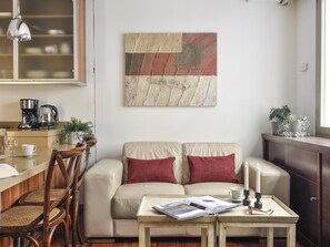 A living room with a sofa, two red cushions, a coffee table with a magazine, a coffee maker, and a potted plant. - Luxury Studio in Plaza de Colon (Madrid)