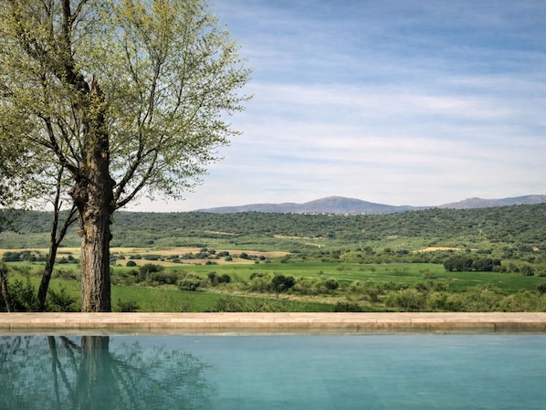 Ein Pool mit Blick auf einen Baum und eine Landschaft mit Hügeln.