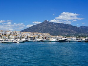 Ein Yachthafen mit vertäuten Booten, eine Küstenstadt mit weißen Gebäuden und ein Berg im Hintergrund.