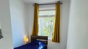 Ett litet, ljust rum med en säng, ett fönster med gula gardiner och en taklampa.