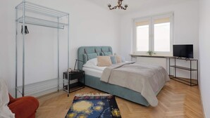 A bedroom with a bed, a TV, a shelf, a wardrobe, and a chandelier. - Stylish Apartment with Balcony | Center of Warsaw (Warszawa)
