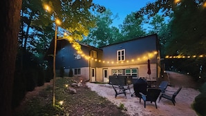 Et hus med terrasse, udendørs møbler og lyskæder.