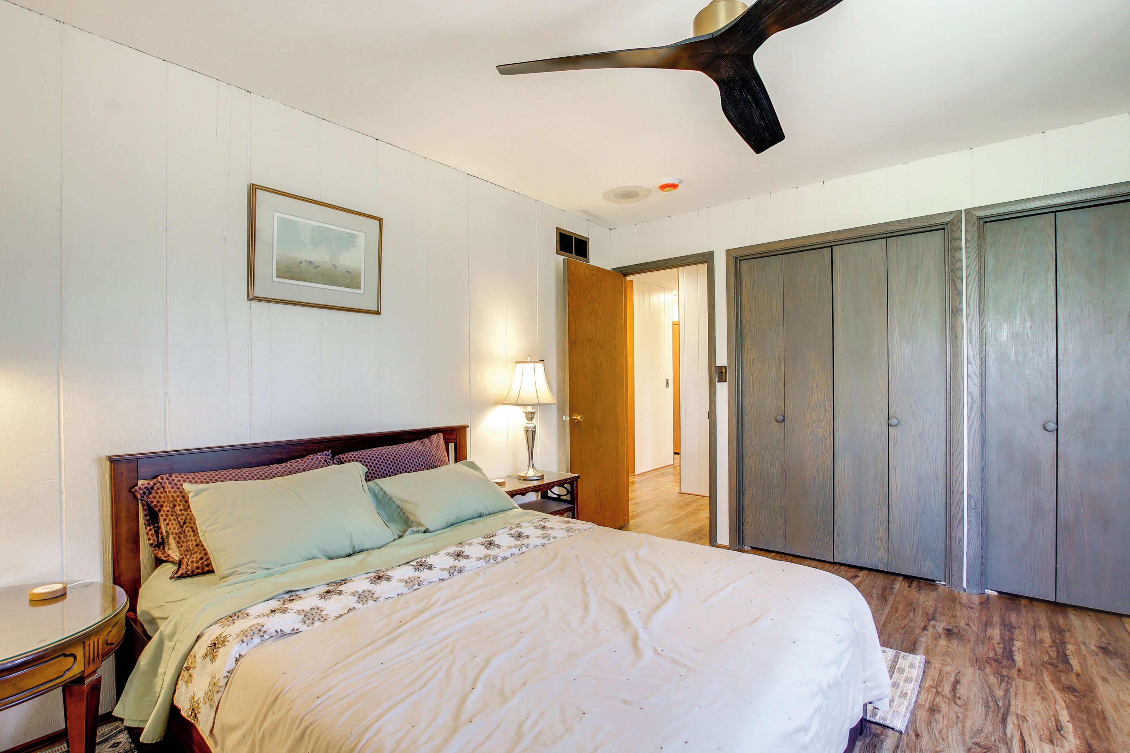Ein Schlafzimmer mit Bett, Nachttisch, Lampe, Kleiderschrank und Deckenventilator.