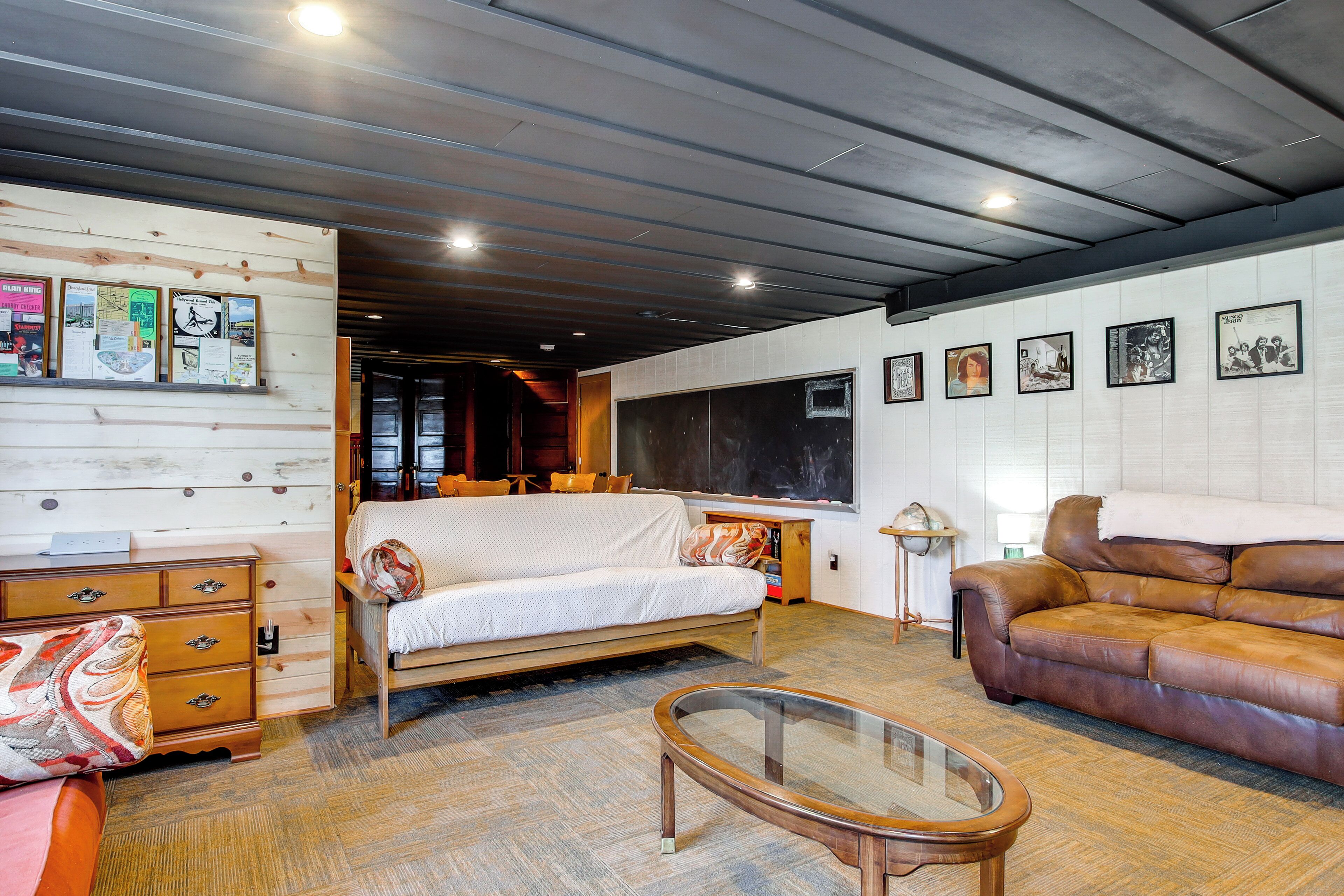 A room with a wooden dresser, a sofa, a leather couch, a glass coffee table, and a large window.