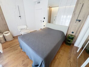 Ein Schlafzimmer mit einem Bett, einem Sessel, einer Tür und einem Spiegel.