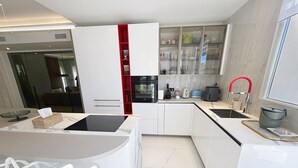 A modern kitchen with white cabinetry, a red accent wall, and a dining area with white chairs. - Apartment  by Interhome (Cannes)