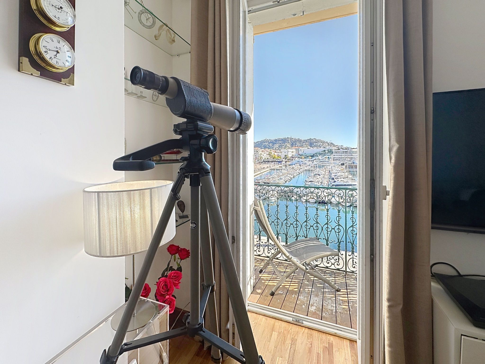 Un telescopio su un treppiede, una lampada e un balcone con vista su un porto turistico e degli edifici.